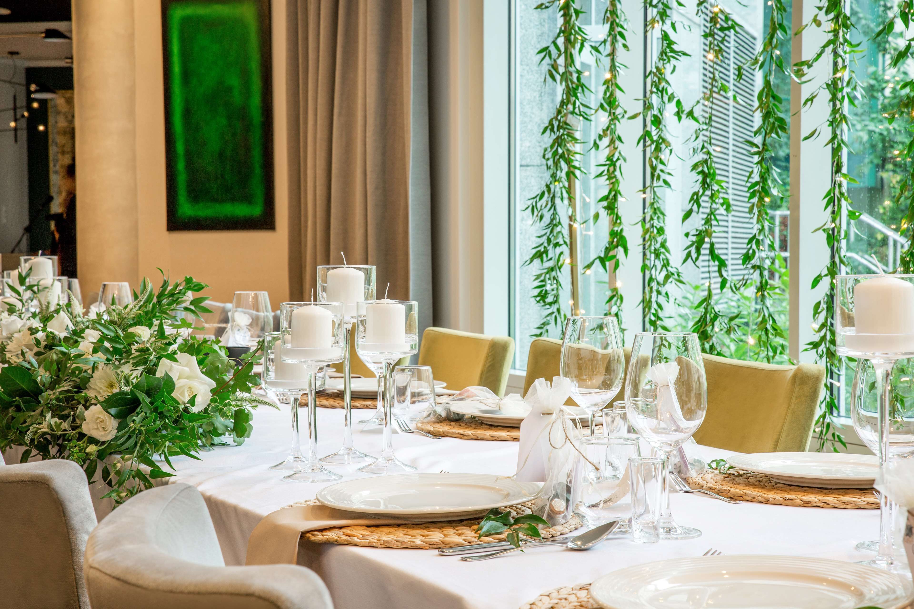 A dining table set with white tablecloths, candles, and glassware, surrounded by chairs with beige upholstery.