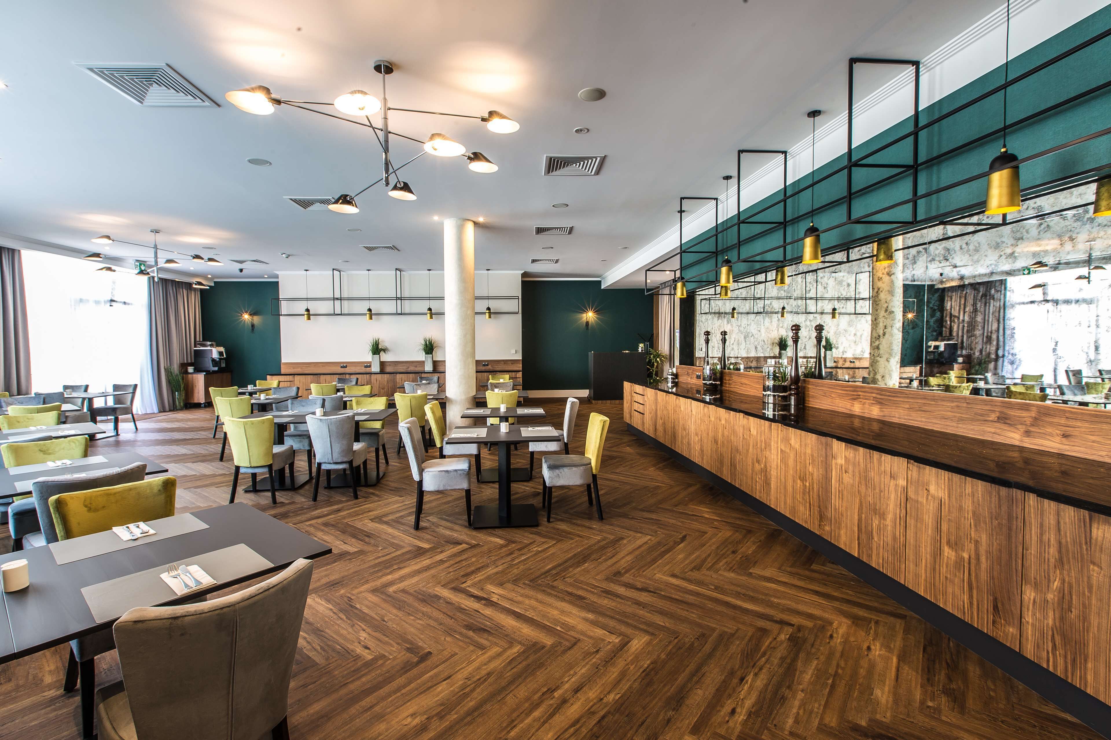 Een modern restaurant met houten vloeren, gele en grijze stoelen, en een bar met een marmeren aanrecht.