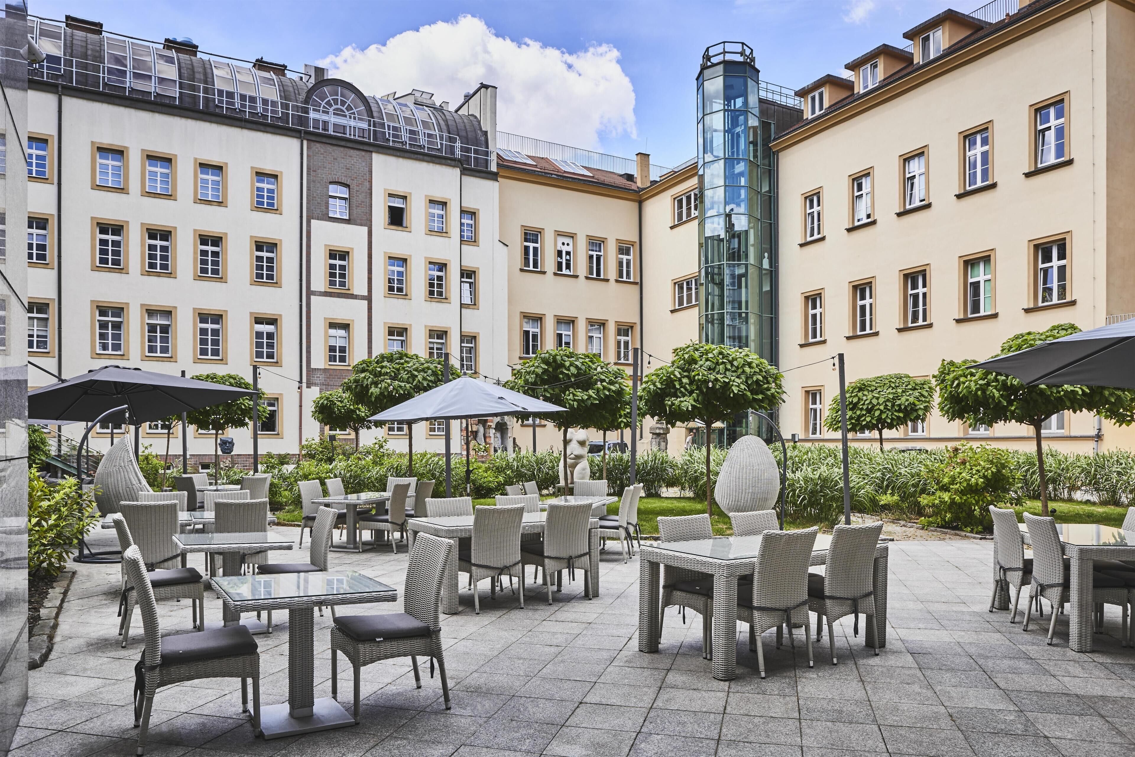 Eine Außenpatio-Terrasse mit Korbmöbeln und Sonnenschirmen, umgeben von Gebäuden mit zahlreichen Fenstern und Balkonen.