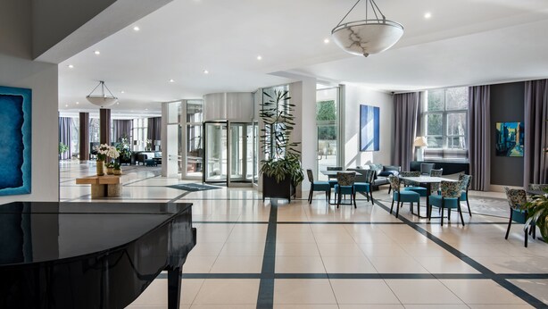 A spacious hotel lobby with a grand piano, modern furniture, and large windows offering views of the outdoors. - Radisson Blu Hotel, Wroclaw (Wroclaw)