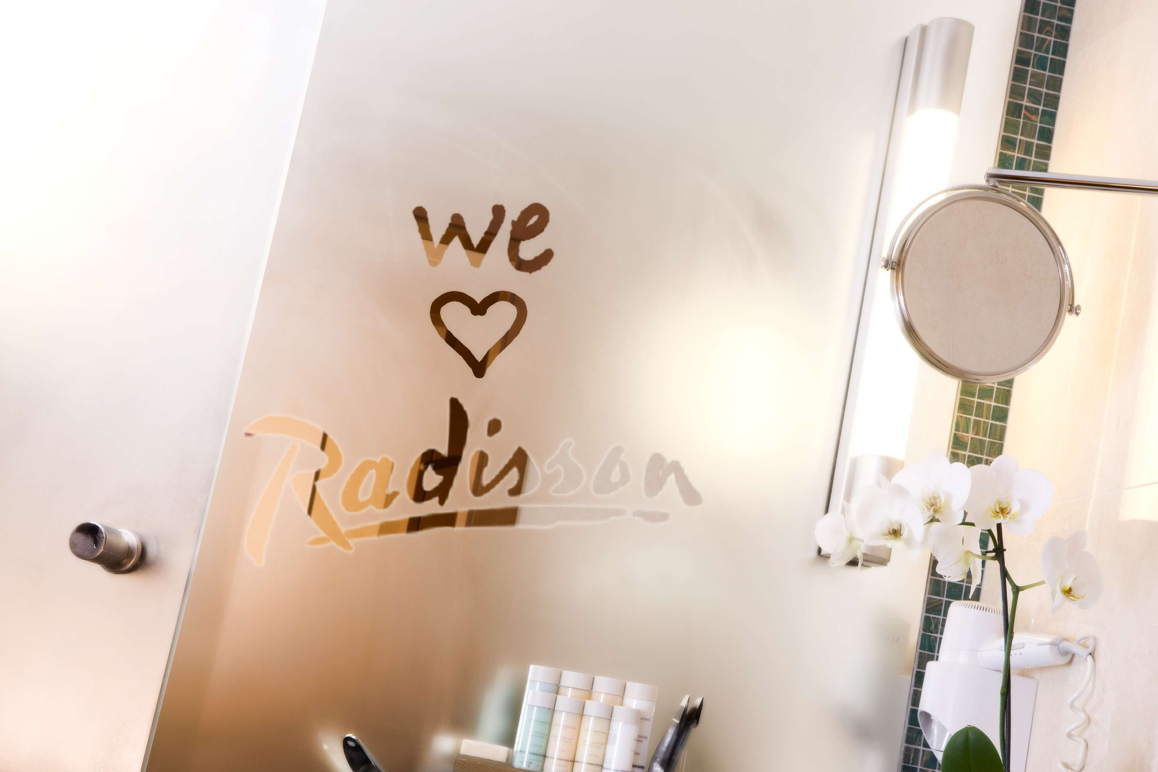 Une salle de bain avec un miroir, un porte-serviettes et un mur sur lequel est inscrit le texte : « Nous aimons Radisson. »