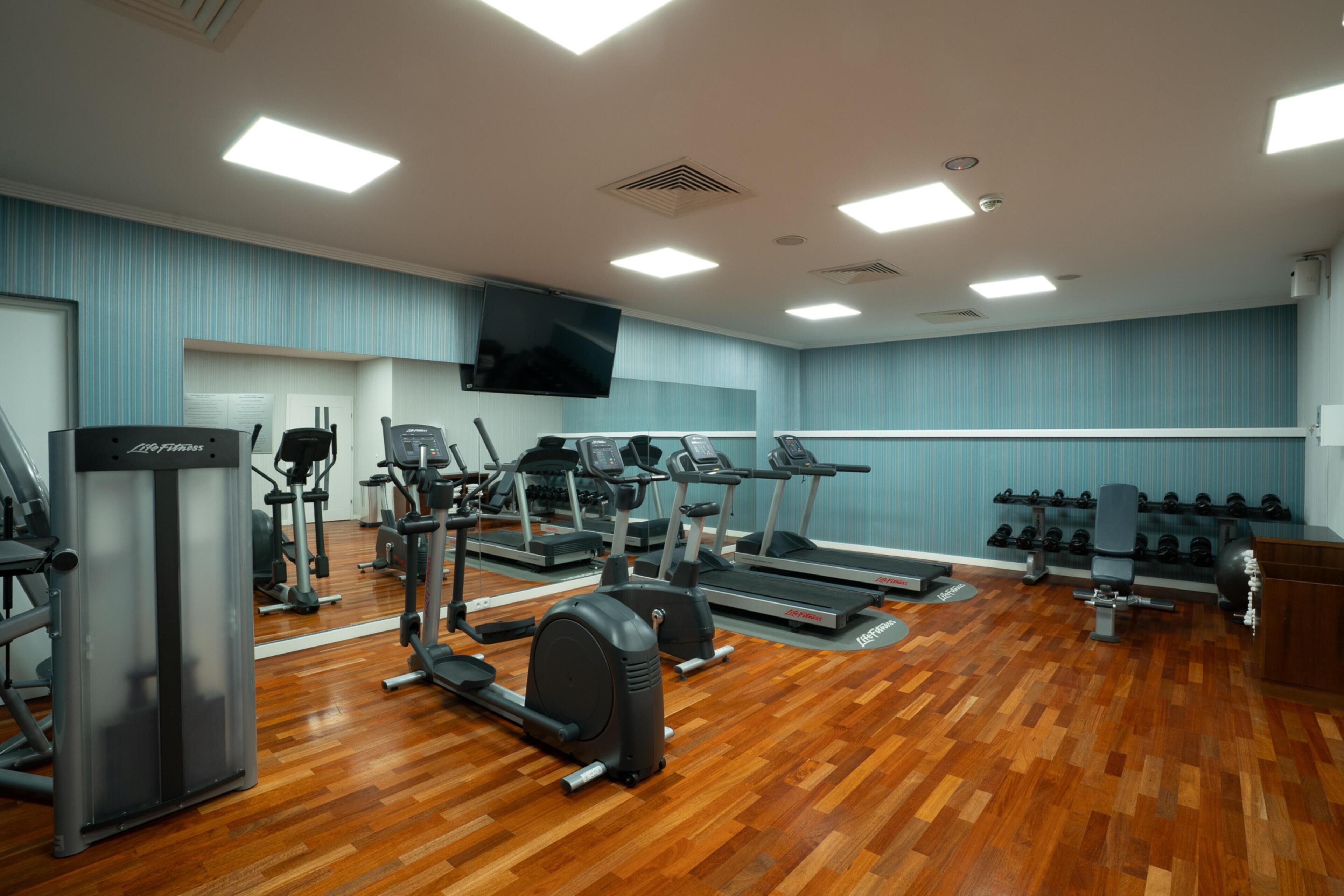 A gym with treadmills, elliptical machines, weight benches, and dumbbells.