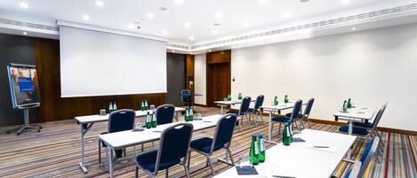 A conference room with tables, chairs, a projector screen, and a carpeted floor.
