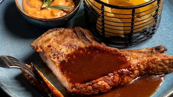 Un plato con un trozo de carne, un bol de salsa y una cesta de papas fritas.
