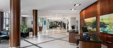 A spacious lobby with a central seating area, a reception desk, and a large painting on the wall.