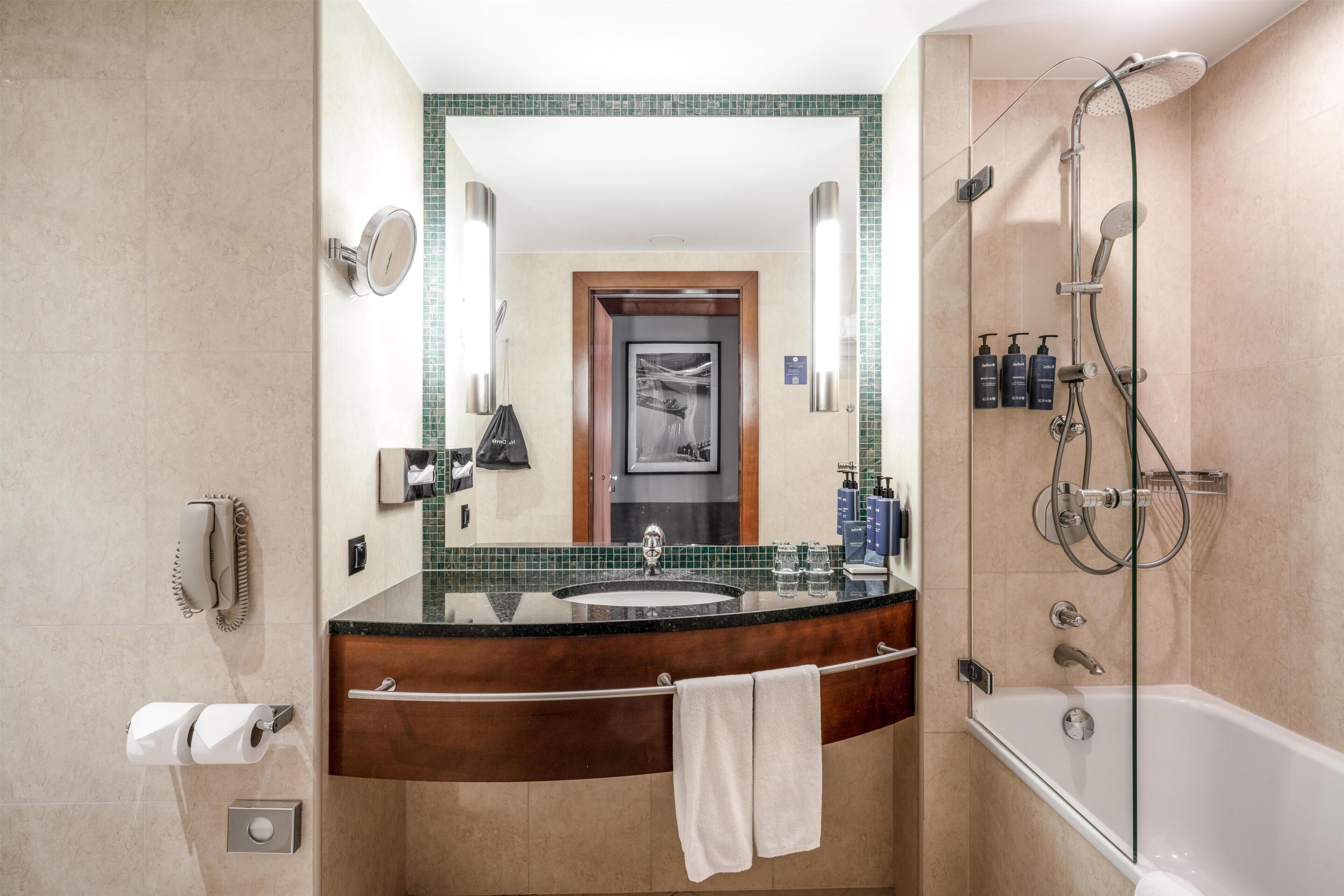 Un baño con un espejo grande, lavamanos, ducha e inodoro.