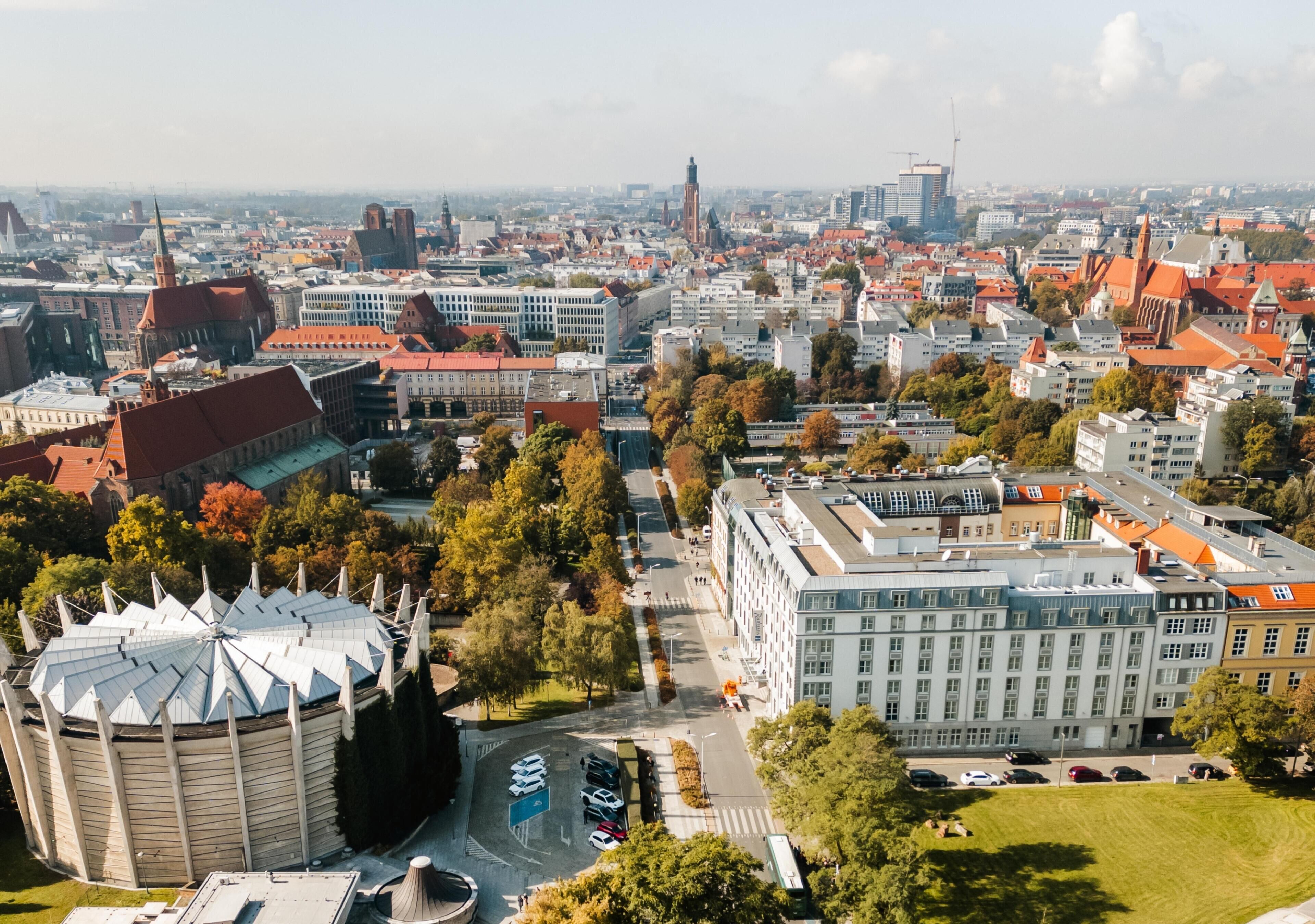 A cityscape with a mix of historical and modern buildings, including a prominent tower and a large circular structure.
