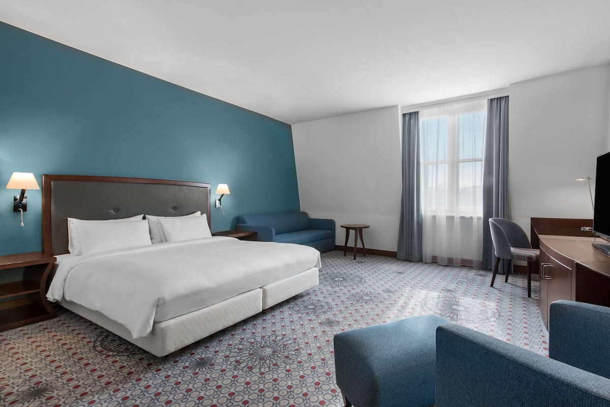 Habitación de hotel con cama, escritorio, silla, sofá y televisor.