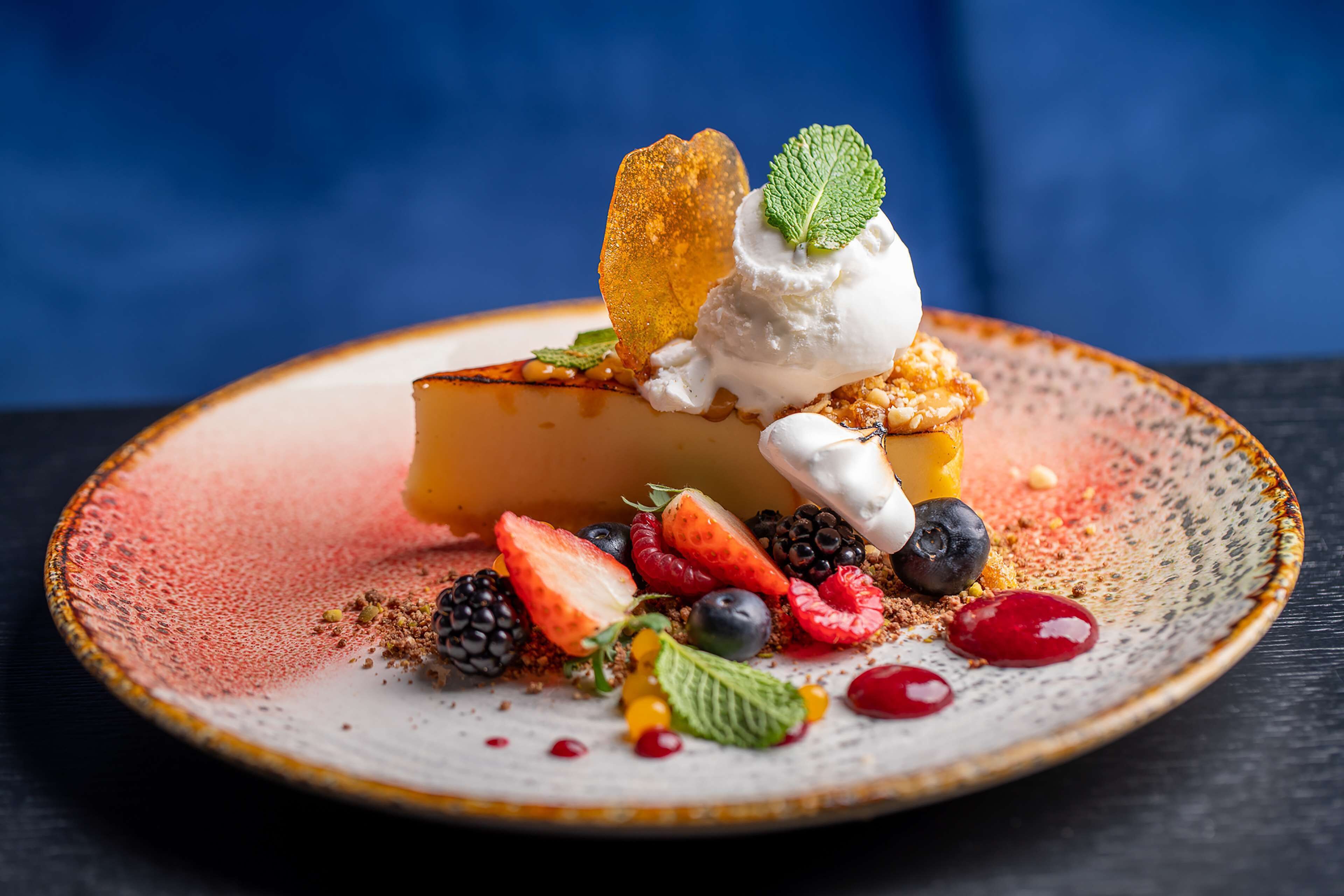 A dessert on a ceramic plate with various fruits and a mint leaf.