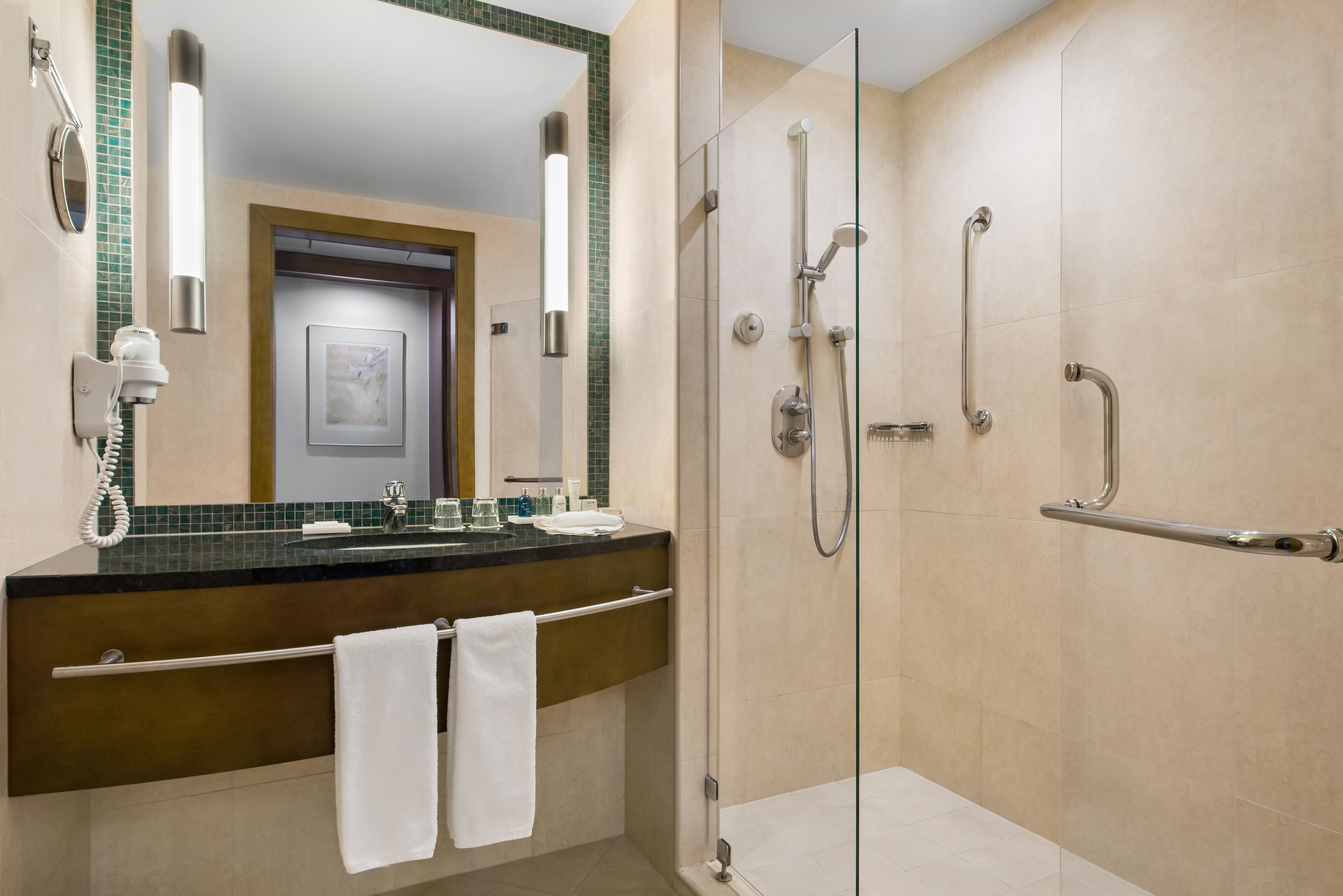 Een moderne badkamer met een glazen douchecabine, een wastafelmeubel met handdoekhouder en een spiegel met wandlampen.