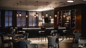 A dimly lit bar area with hanging pendant lights, a bar counter, and a selection of bottles on shelves. - Radisson Blu Hotel, Wroclaw (Wroclaw)