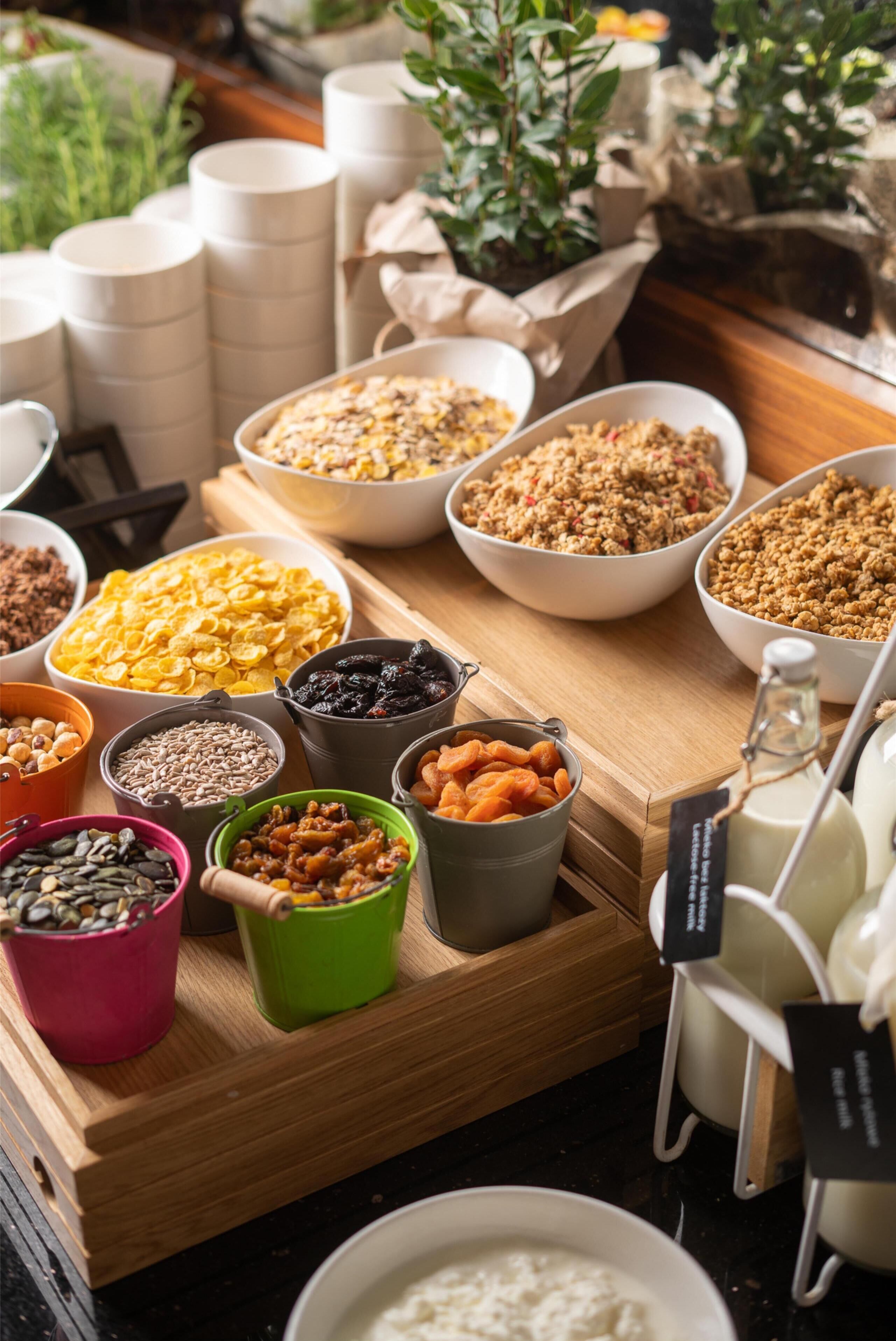 On peut voir une variété d’aliments et de récipients sur une table en bois, notamment des bols de céréales, des noix et des fruits secs.