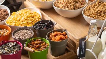 On peut voir une variété d’aliments et de récipients sur une table en bois, notamment des bols de céréales, des noix et des fruits secs.
