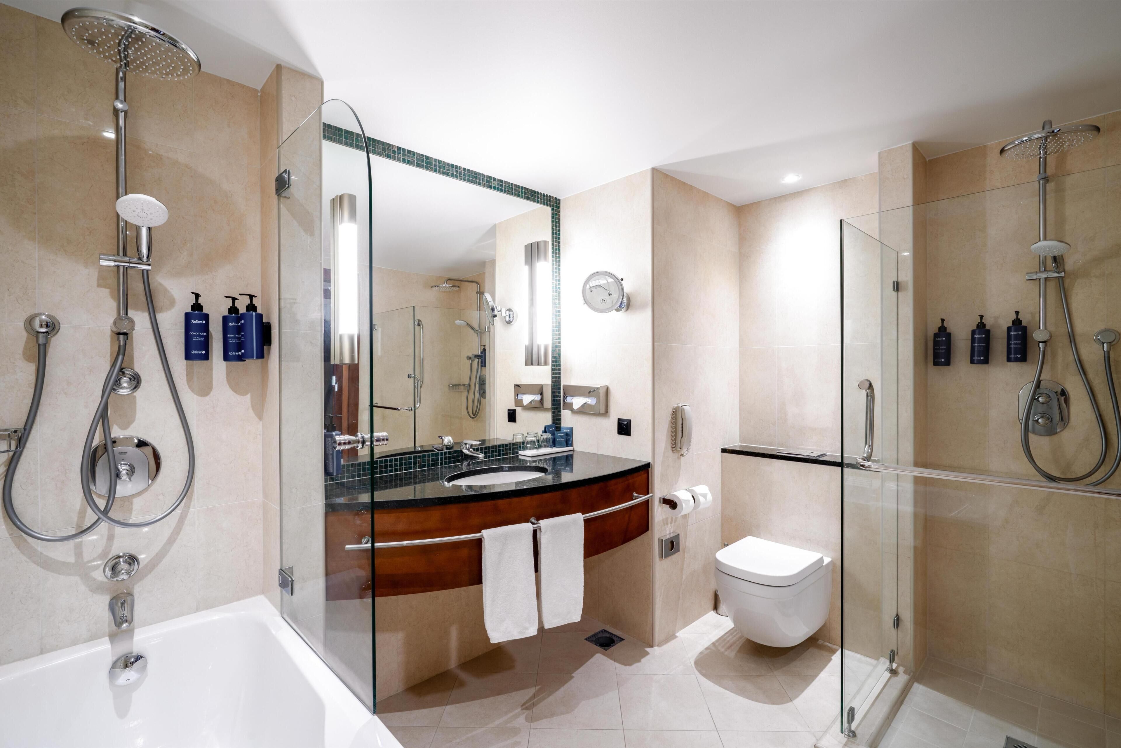 A modern bathroom with a glass-enclosed shower, a bathtub, a toilet, and a vanity with a mirror.