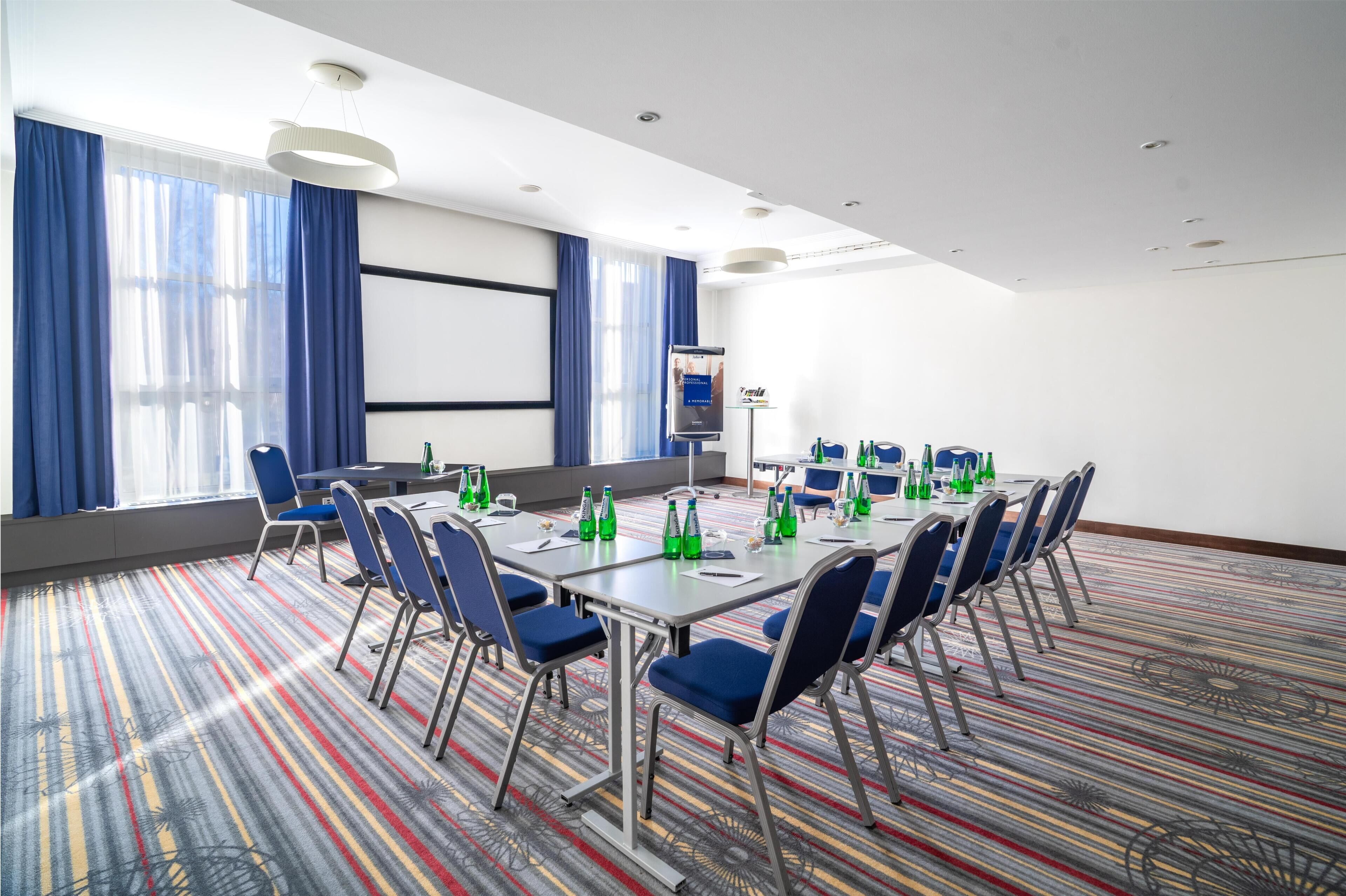A conference room with a long table, chairs, and a projector screen.