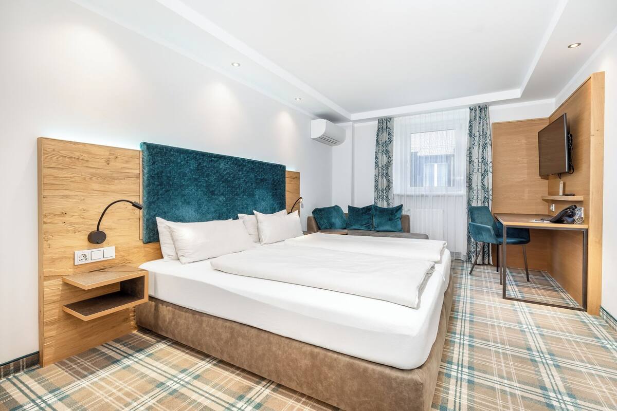 A hotel room with a large bed, a desk, a TV, and a window with curtains.