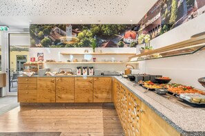 A buffet setup with a variety of food items, wooden cabinetry, and a large poster on the wall. - Hotel zur Post (Ismaning)