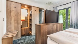 A bedroom with a bed, a TV on a wooden stand, a closet with a mirror, and a window with curtains. - Hotel zur Post (Ismaning)