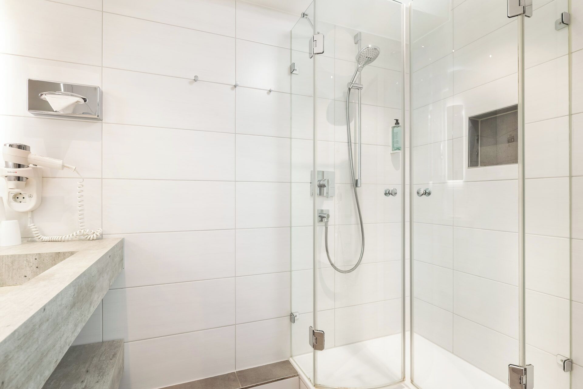 Un baño moderno con ducha de vidrio, tocador de mármol y secador de pelo en la pared.