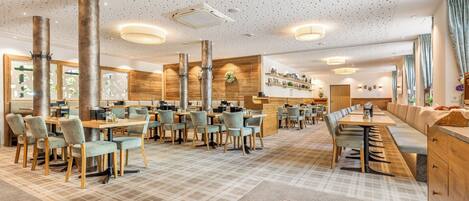 Un restaurant spacieux avec de hauts plafonds, des éléments décoratifs en bois et différents types de mobilier pour créer des espaces de détente variés.
