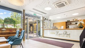 A hotel reception area with a modern design, featuring a reception desk, seating area, and a view of the outdoor garden. - Hotel zur Post (Ismaning)