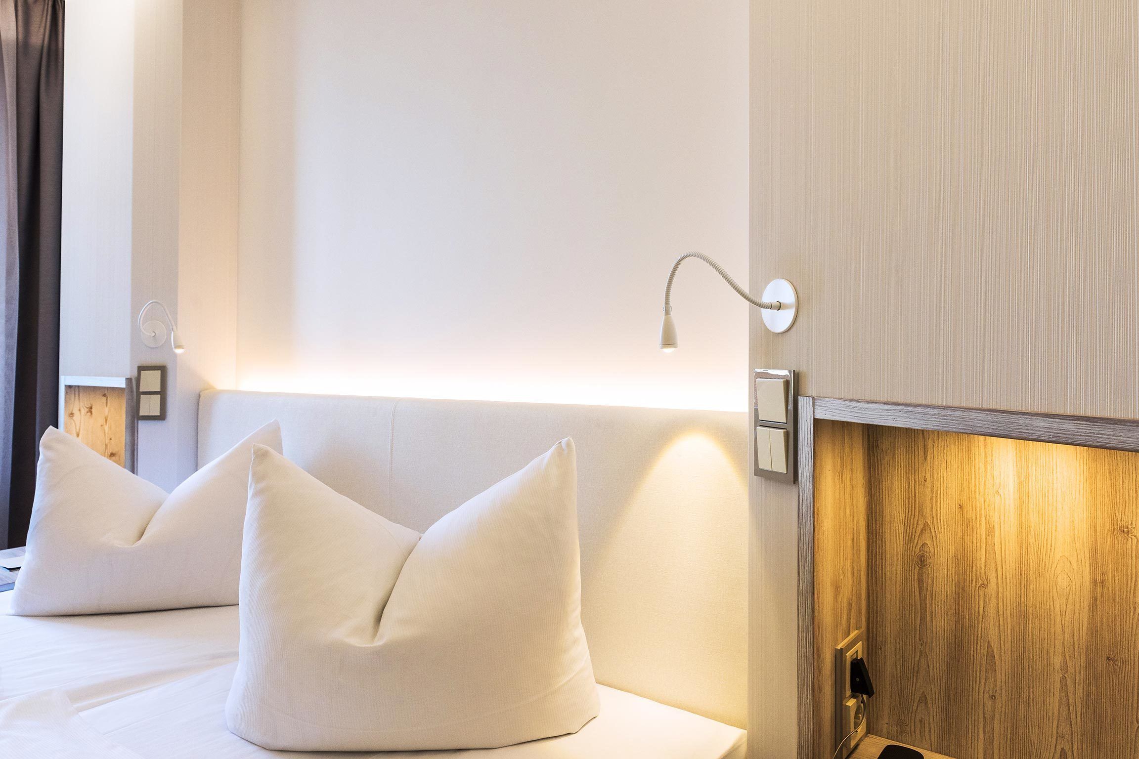 Ein Hotelzimmer mit einem Bett, zwei Kissen, einem Nachttisch, einer Lampe und einer Holzvertäfelung an der Wand.