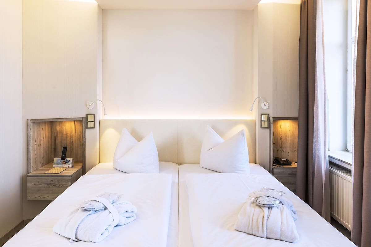 A hotel room with two beds, bedside tables with lamps, and a window with curtains.