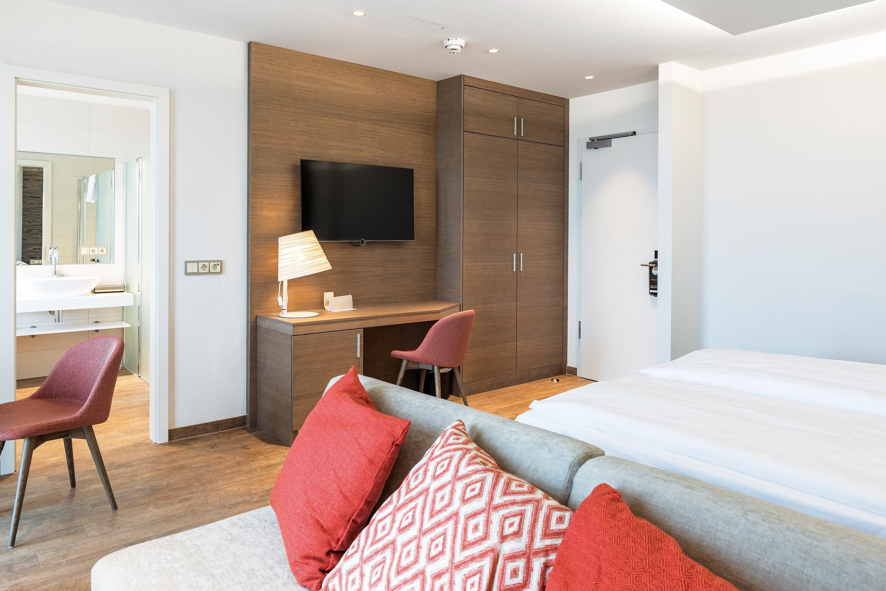 Una habitación de hotel moderna con cama, escritorio, televisor y zona de estar con sofá y sillones.