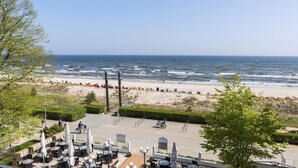 Vista frente a la playa con mesas al aire libre, un camino para bicicletas y vista al océano.