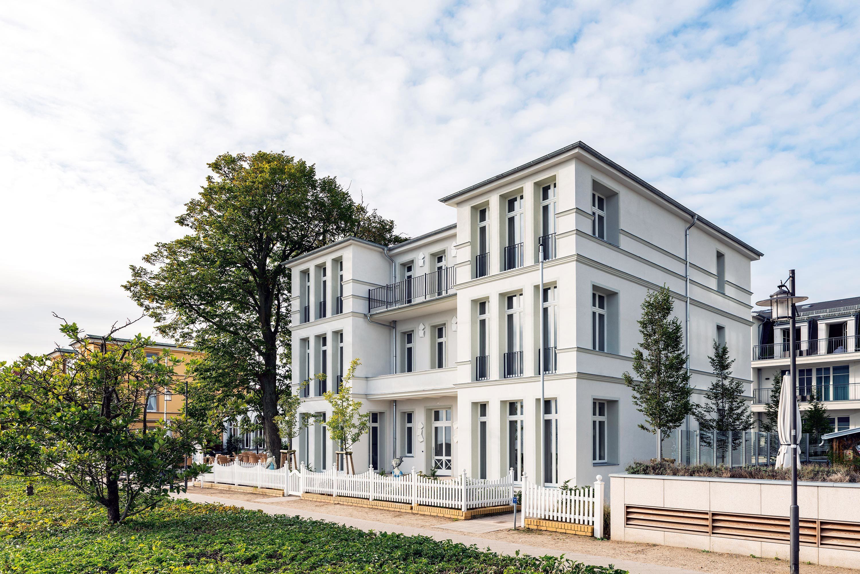 A multi-story building with a white facade, large windows, and a white fence in front.