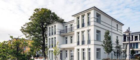 A multi-story building with a white facade, large windows, and a white fence in front.