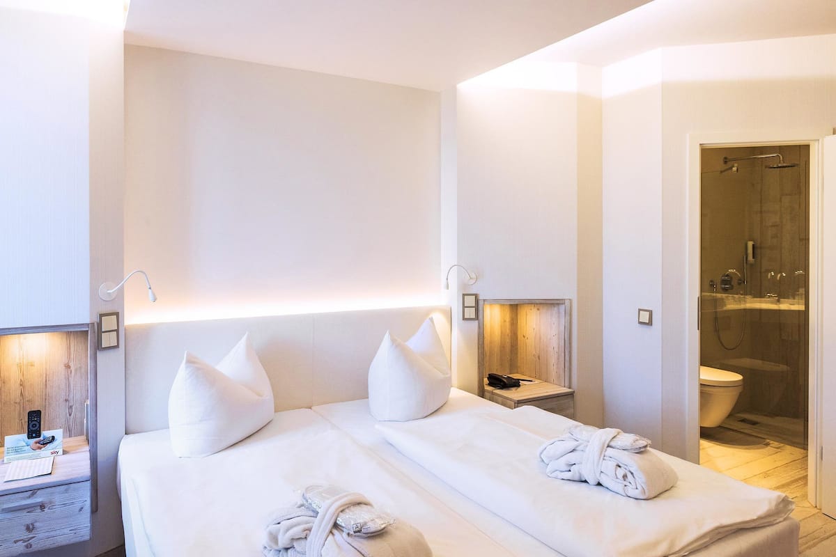 A hotel room with a bed, bedside tables, a nightstand, a shower area, and a toilet.