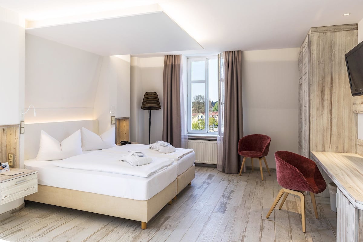 A modern hotel room with a large bed, a desk, two red chairs, and a TV.