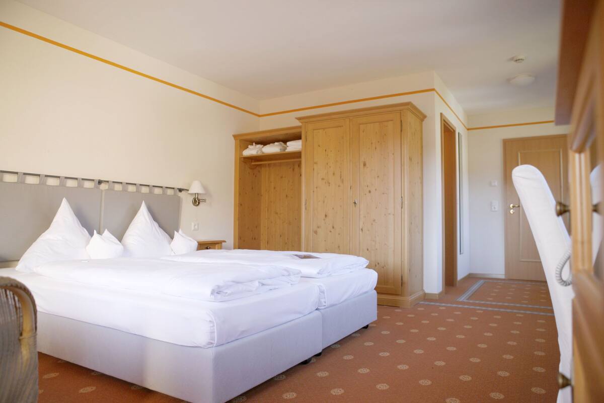 A hotel room with a large bed, wooden wardrobe, and a bathroom with a shower curtain.