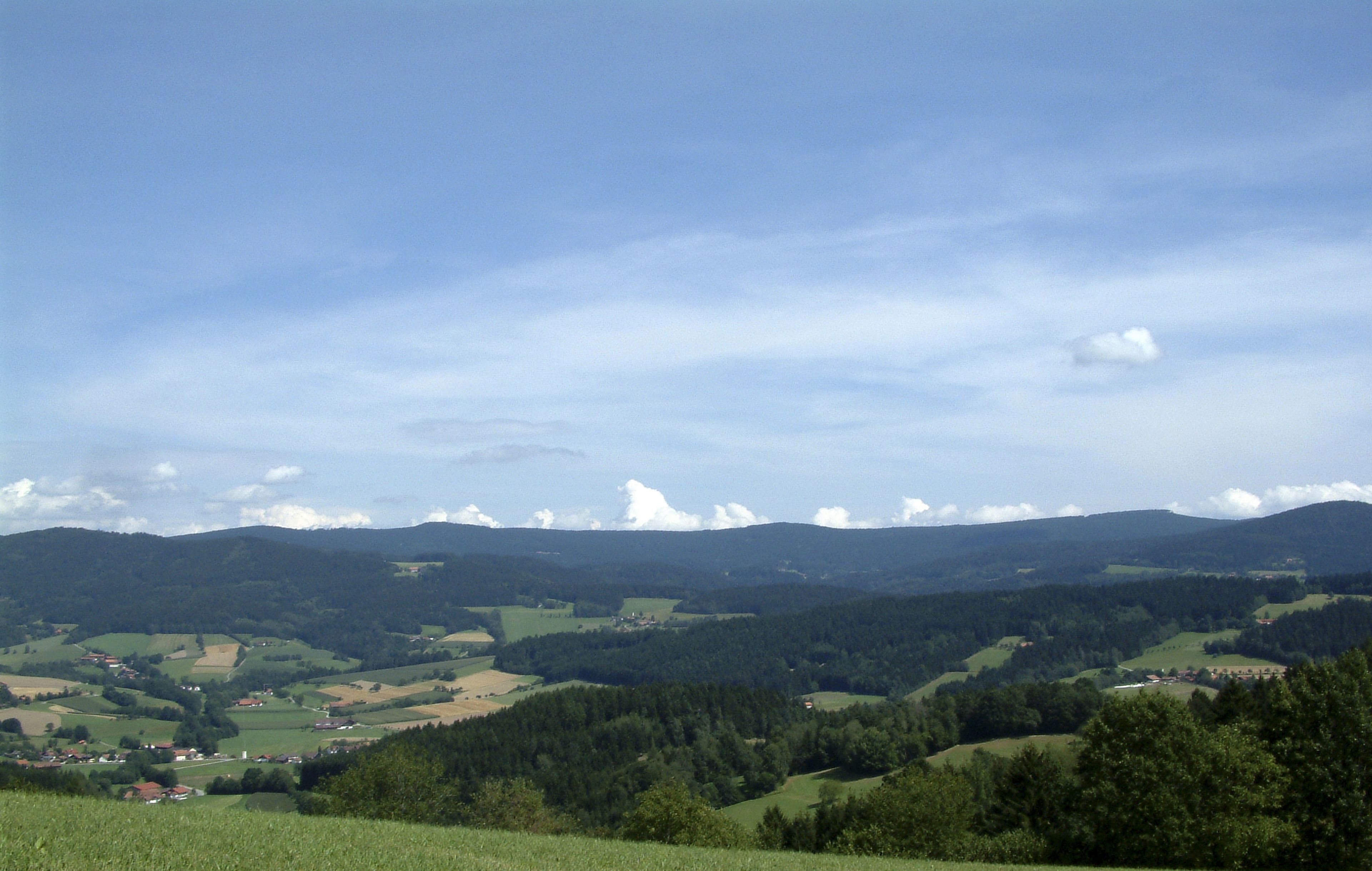 Une vue panoramique d’une vallée avec des collines ondoyantes, des maisons dispersées et un ciel dégagé.