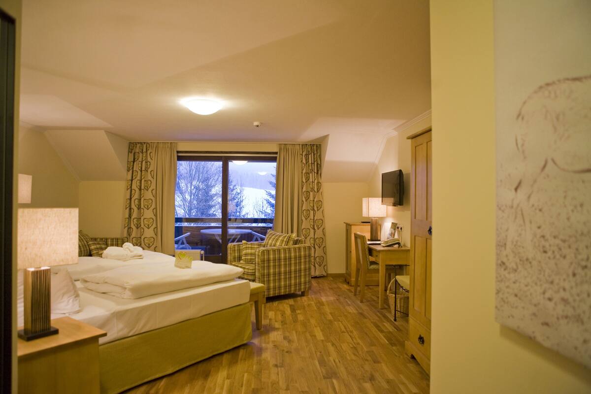 A hotel room with a bed, a desk, a chair, a window with curtains, and a television on the wall.