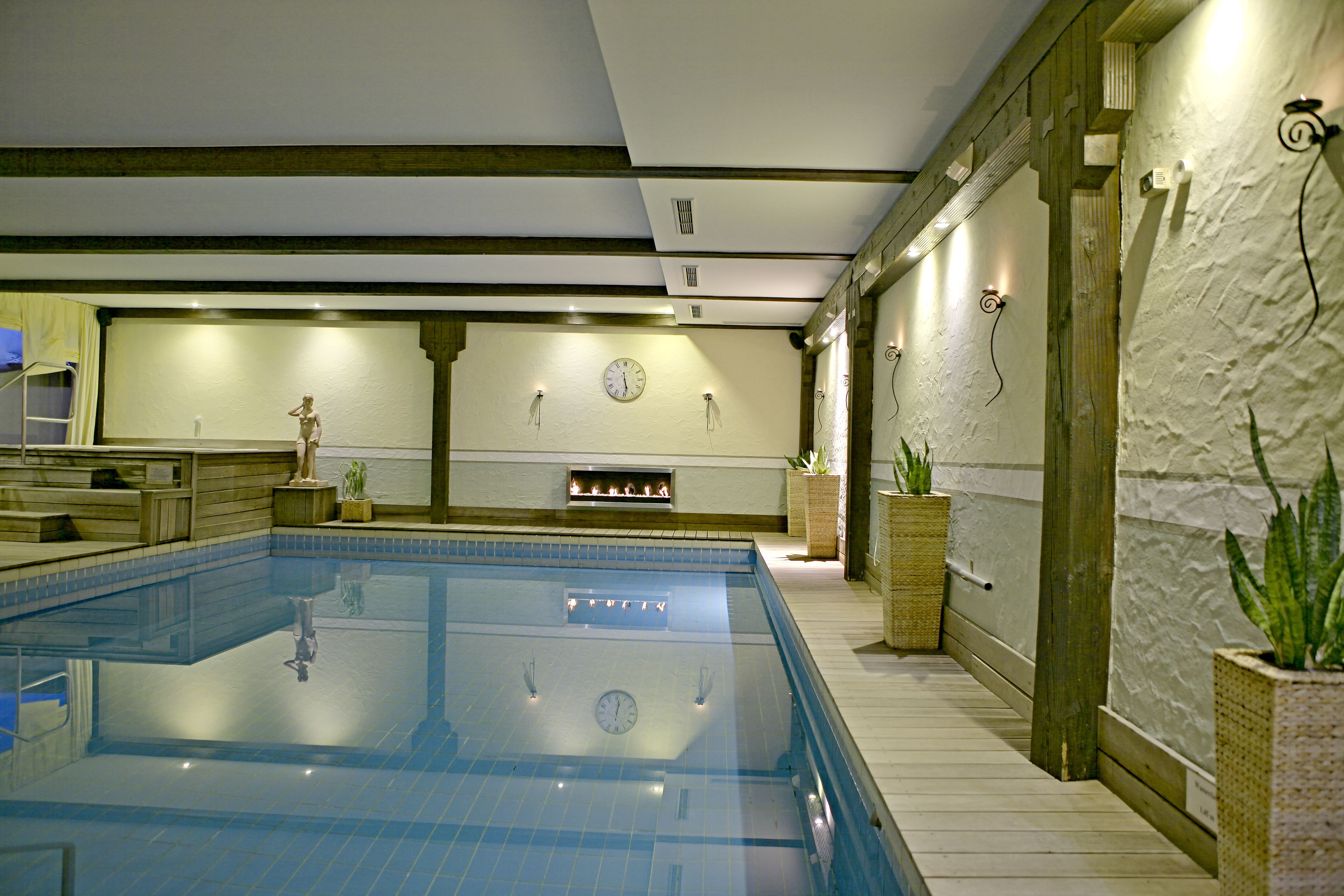 A swimming pool with a clock on the wall, wooden beams, and potted plants.