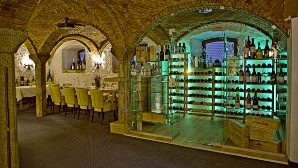 Una bodega con techos de ladrillo abovedados, una vitrina de vidrio con botellas de vino y un comedor con sillas y mesas amarillas.