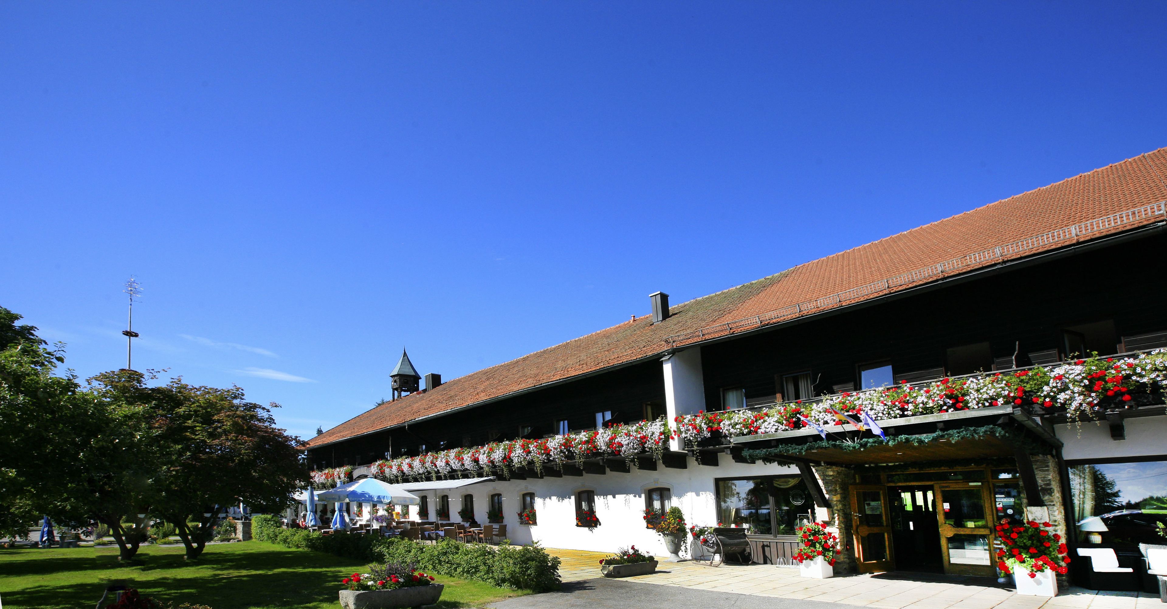A traditional building with a balcony adorned with flowers, a clear blue sky, and a well-maintained garden area.