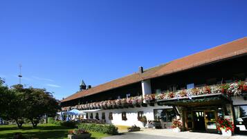 A traditional building with a balcony adorned with flowers, a clear blue sky, and a well-maintained garden area.