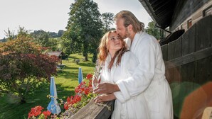 Una pareja parada junto a una barandilla de madera con vistas a un jardín con flores rojas y un banco.