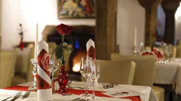 A dining table set with white tablecloths, red napkins, and a red rose centerpiece.
