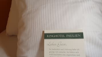 A hotel room with a neatly made bed, a pillow, and a welcome card.