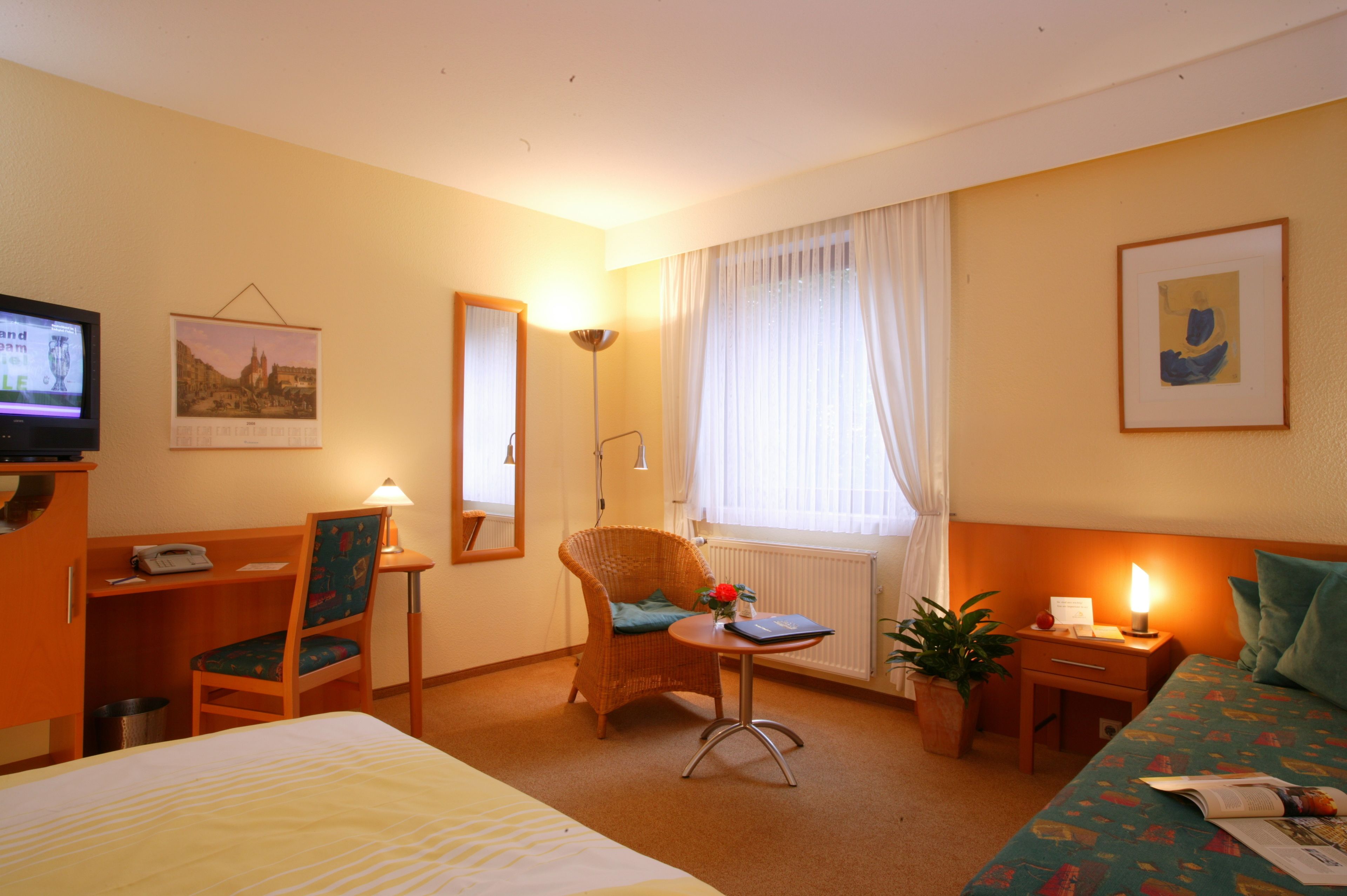 Een hotelkamer met een bed, een stoel, een bureau, een lamp, een potplant en een televisietoestel.