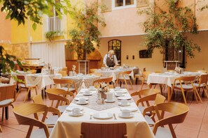 An outdoor dining area with tables set for a meal, surrounded by chairs and potted plants.