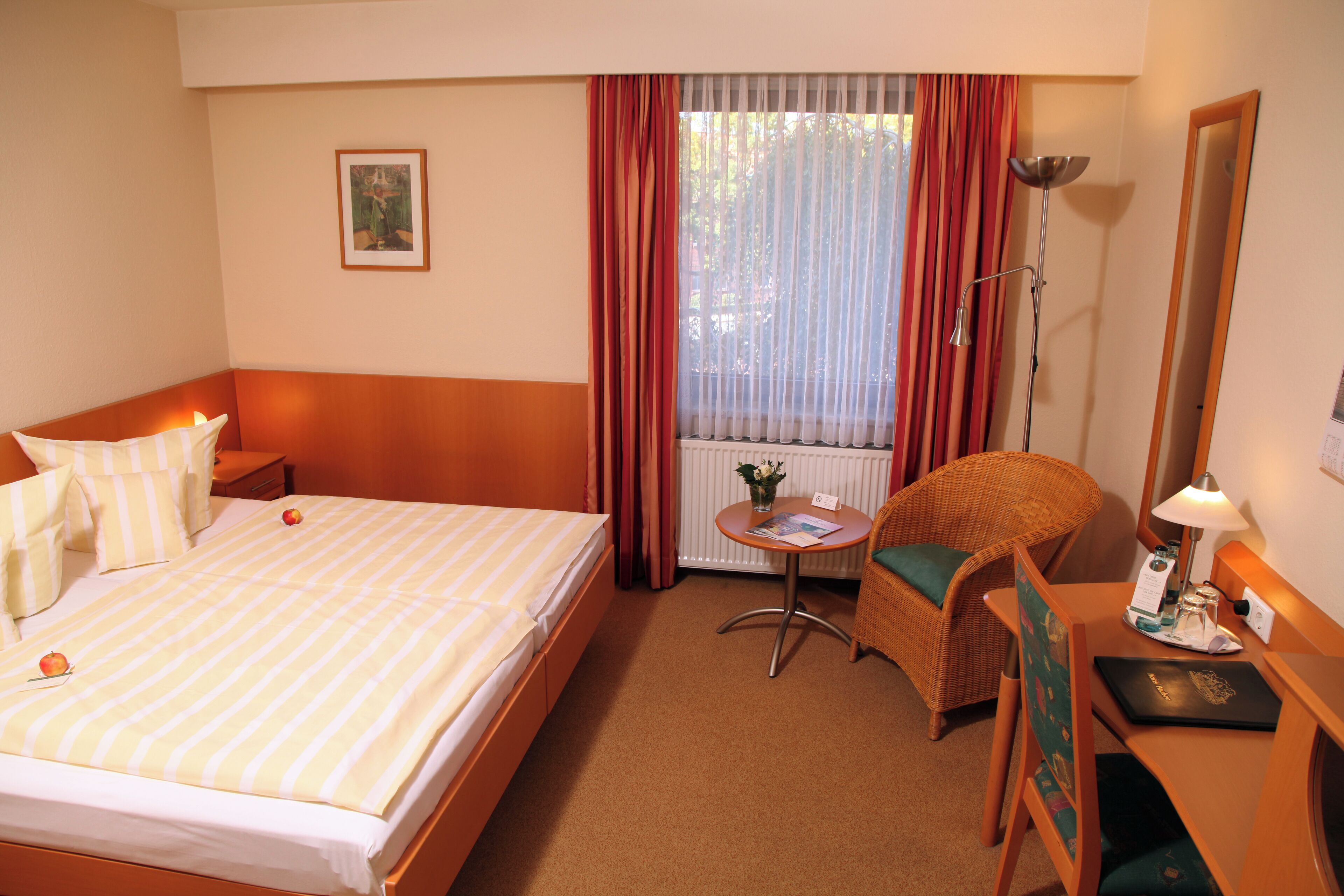 A hotel room with a bed, a desk, a chair, a lamp, and a window with curtains.