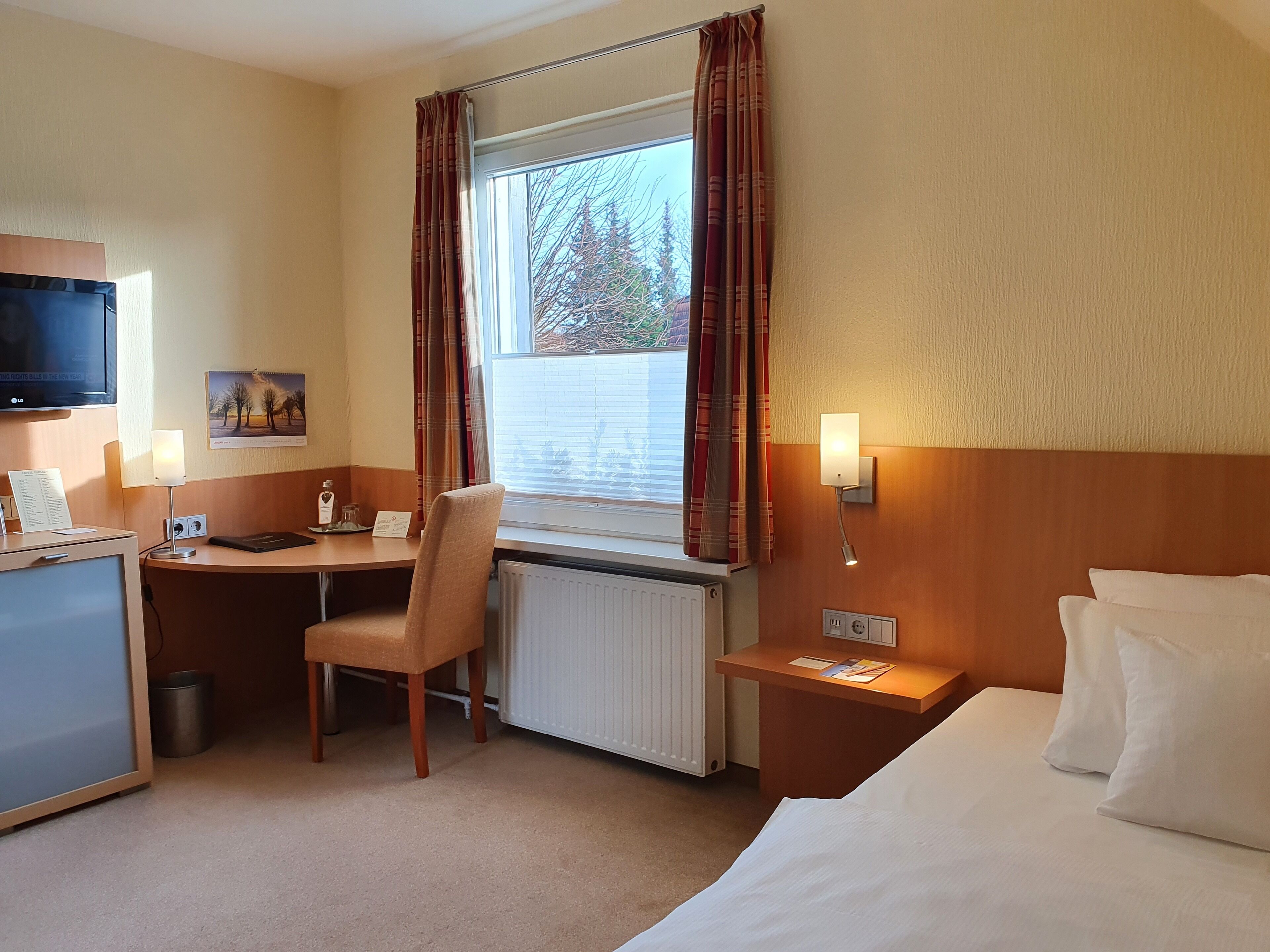 A hotel room with a bed, desk, chair, TV, and window with curtains.
