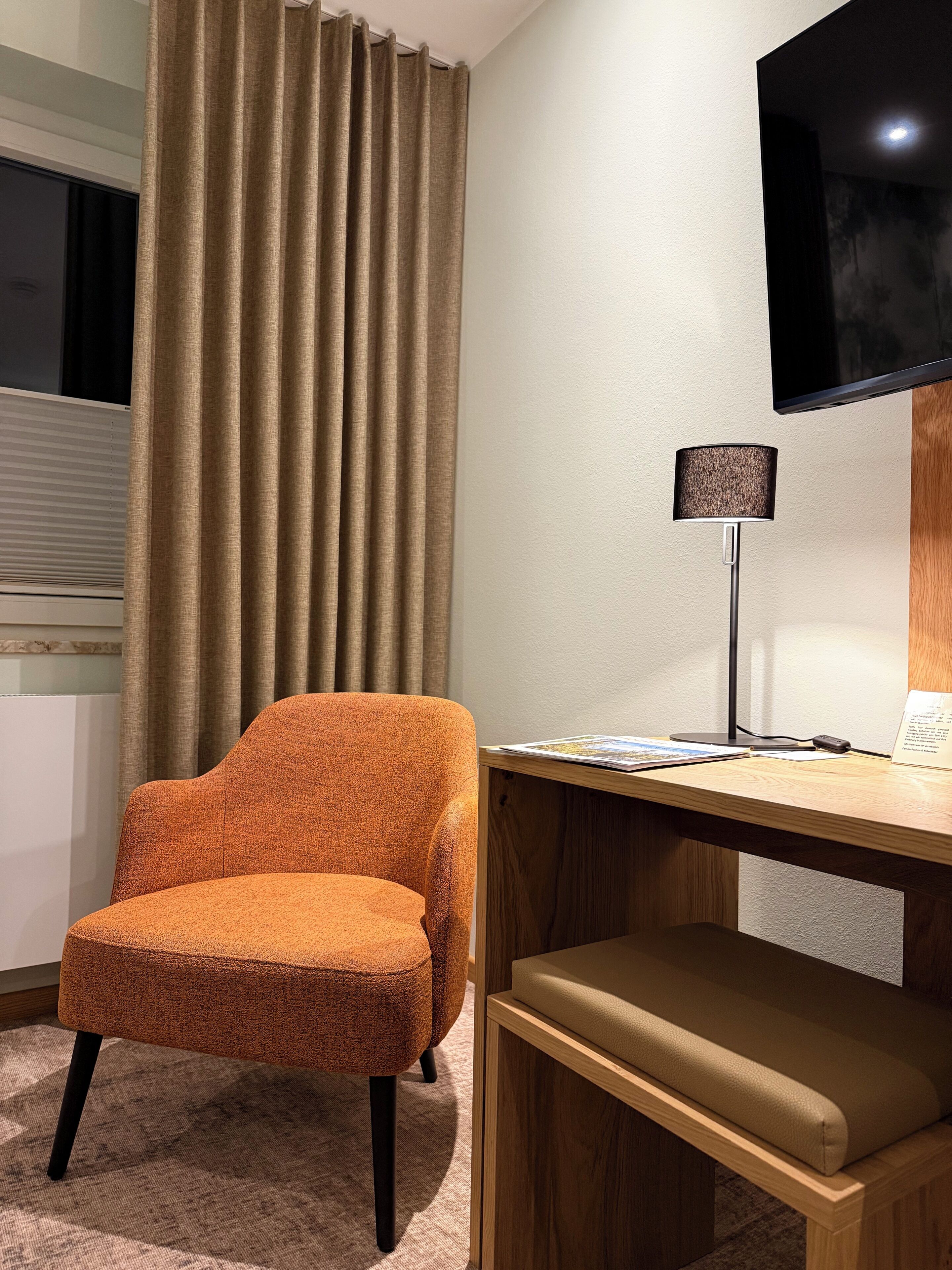 Ein Zimmer mit einem Holztisch, einem Stuhl, einer Lampe und einem an der Wand befestigten Fernseher.