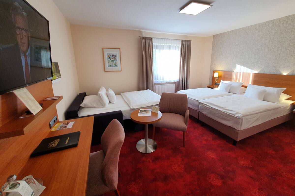 Habitación de hotel con dos camas, un escritorio, una silla, una mesita, televisión y ventana con cortinas.