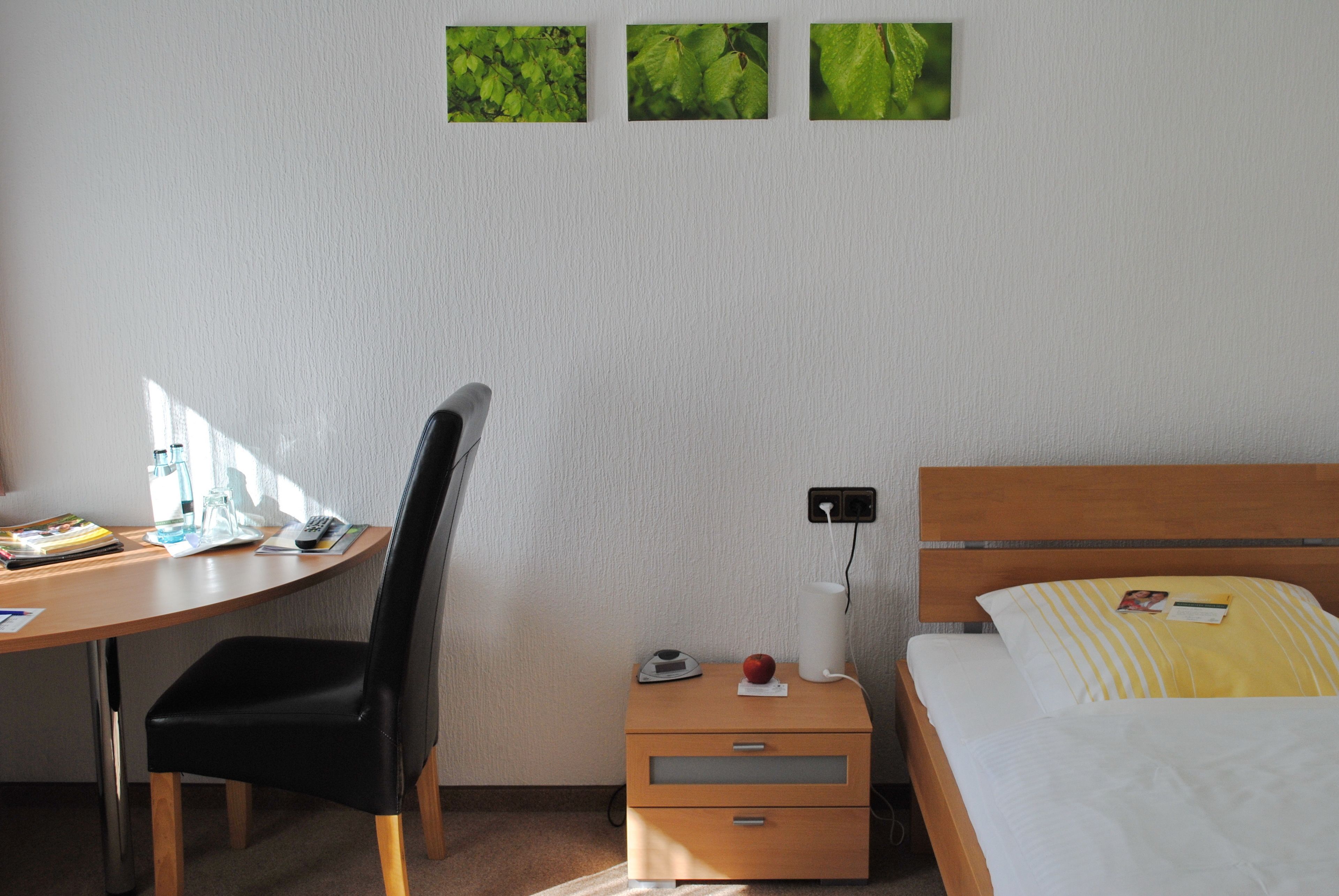 A hotel room with a desk, chair, bedside table, and bed.